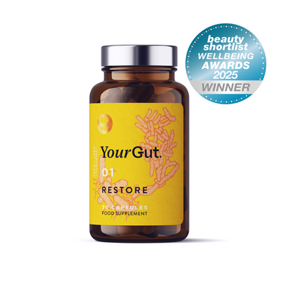 A brown supplement bottle labeled 01 Restore with 30 capsules features an orange probiotic bacteria design on a yellow label. A blue badge reads “Beauty Shortlist Wellbeing Awards 2025 Winner”—an award-winning synbiotic for gut health.